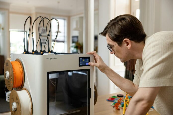 Pria mengoperasikan printer 3D dengan gulungan filamen.