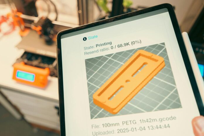 Tablet menampilkan kemajuan cetak 3D dengan printer di latar belakang.